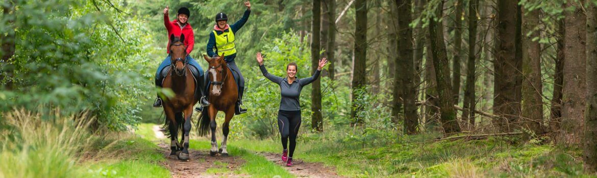 twee vrolijke dames op paard en een juichende hardloopster